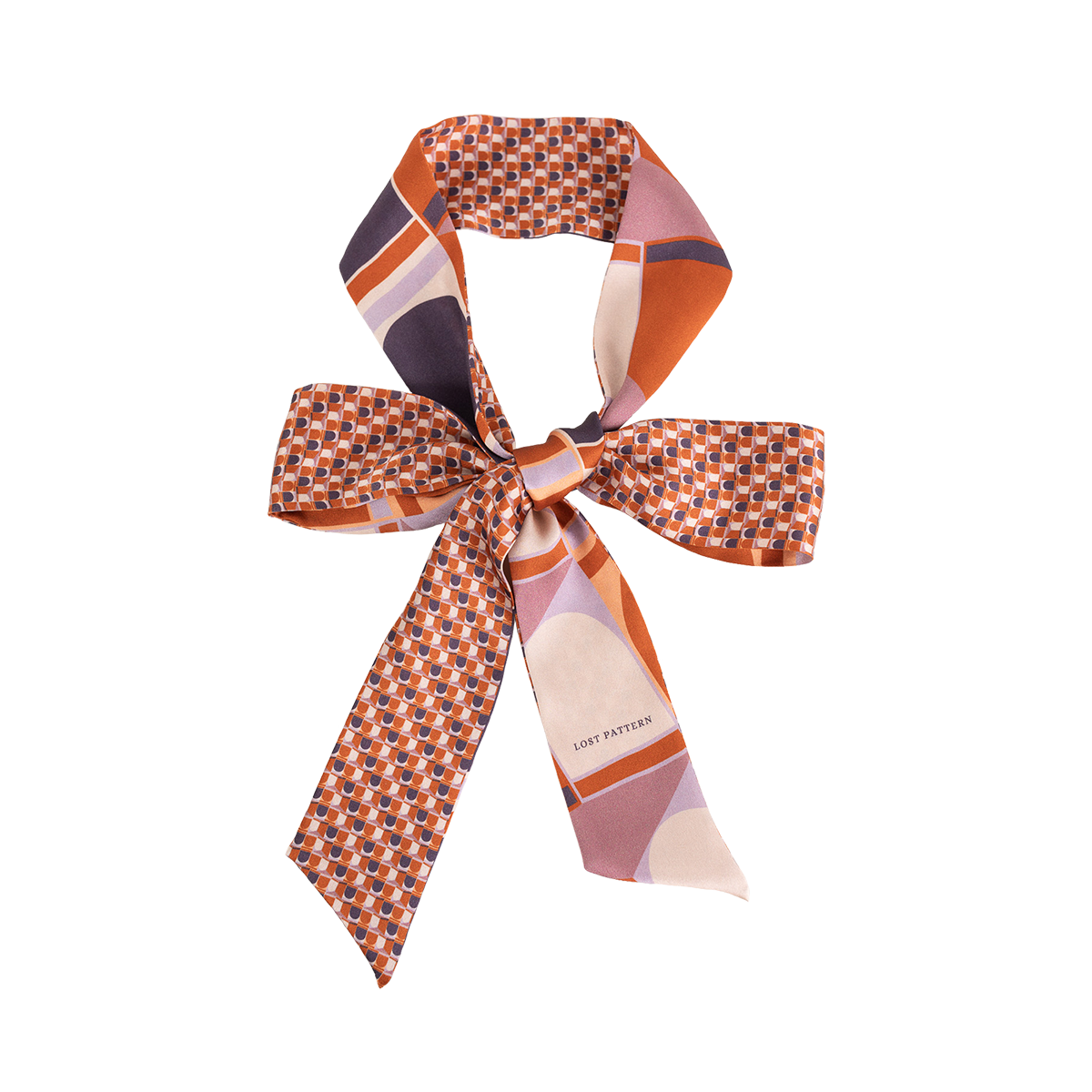 The Silk Skinny Scarf - Clay by Lost Pattern NYC is a double-sided silk satin piece with geometric patterns in orange, purple, and pink—perfect as a chic hair accessory or tied in a bow against a white background.