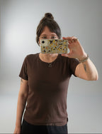 person with brown hair and glasses modeling and taking a selfie of them wearing a brown tee shirt with short sleeves.