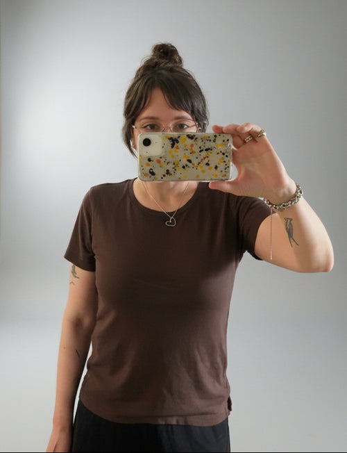 person with brown hair and glasses modeling and taking a selfie of them wearing a brown tee shirt with short sleeves.