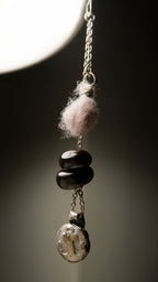 A close-up of the Sunk pendant by Ash Espinoza x Thyne Studio for Thyne Goods, featuring a pink wool ball, three dark oval beads, and a recycled sterling silver charm on a silver chain, crafted in Hyde Park, NY.