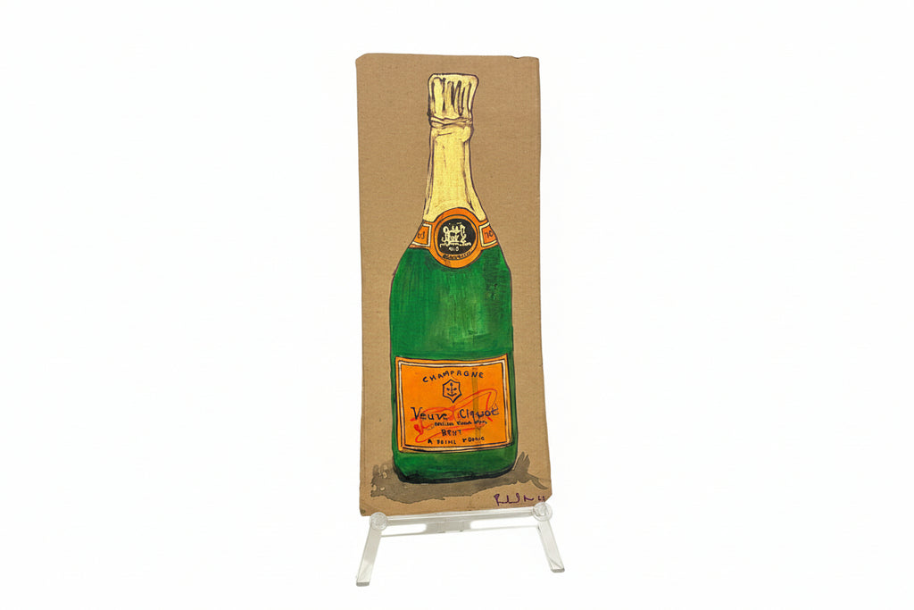 A rectangular cardboard piece titled "Rachel Nelson • Champagne" by Thyne Goods, featuring a painted Veuve Clicquot bottle, stands upright on a clear display against a white background, evoking Rachel Nelson’s immersive art style.
