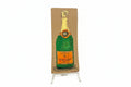 A rectangular cardboard piece titled "Rachel Nelson • Champagne" by Thyne Goods, featuring a painted Veuve Clicquot bottle, stands upright on a clear display against a white background, evoking Rachel Nelson’s immersive art style.