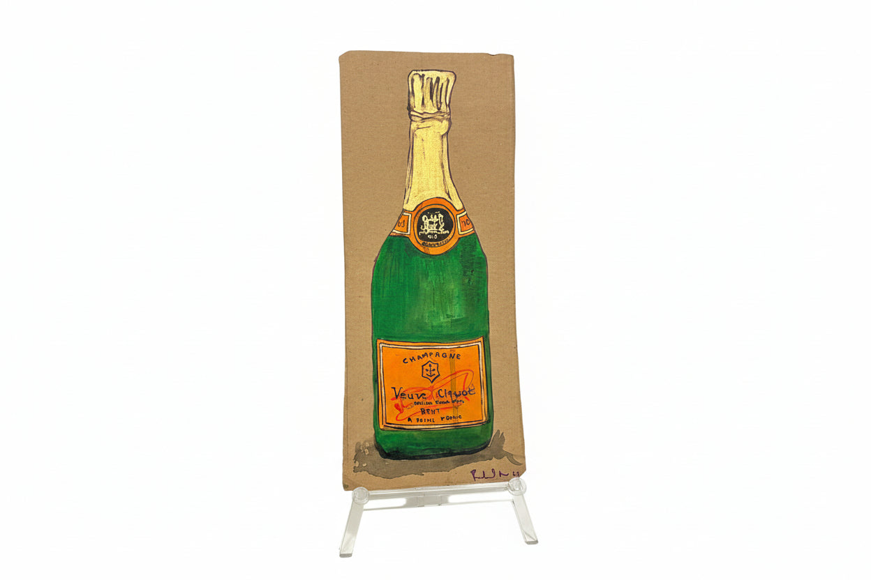 A rectangular cardboard piece titled "Rachel Nelson • Champagne" by Thyne Goods, featuring a painted Veuve Clicquot bottle, stands upright on a clear display against a white background, evoking Rachel Nelson’s immersive art style.