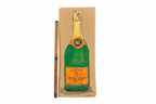 A painted illustration of Thyne Goods Rachel Nelson • Champagne on cardboard is shown next to a wooden ruler for scale, featuring a yellow-orange label and foil.