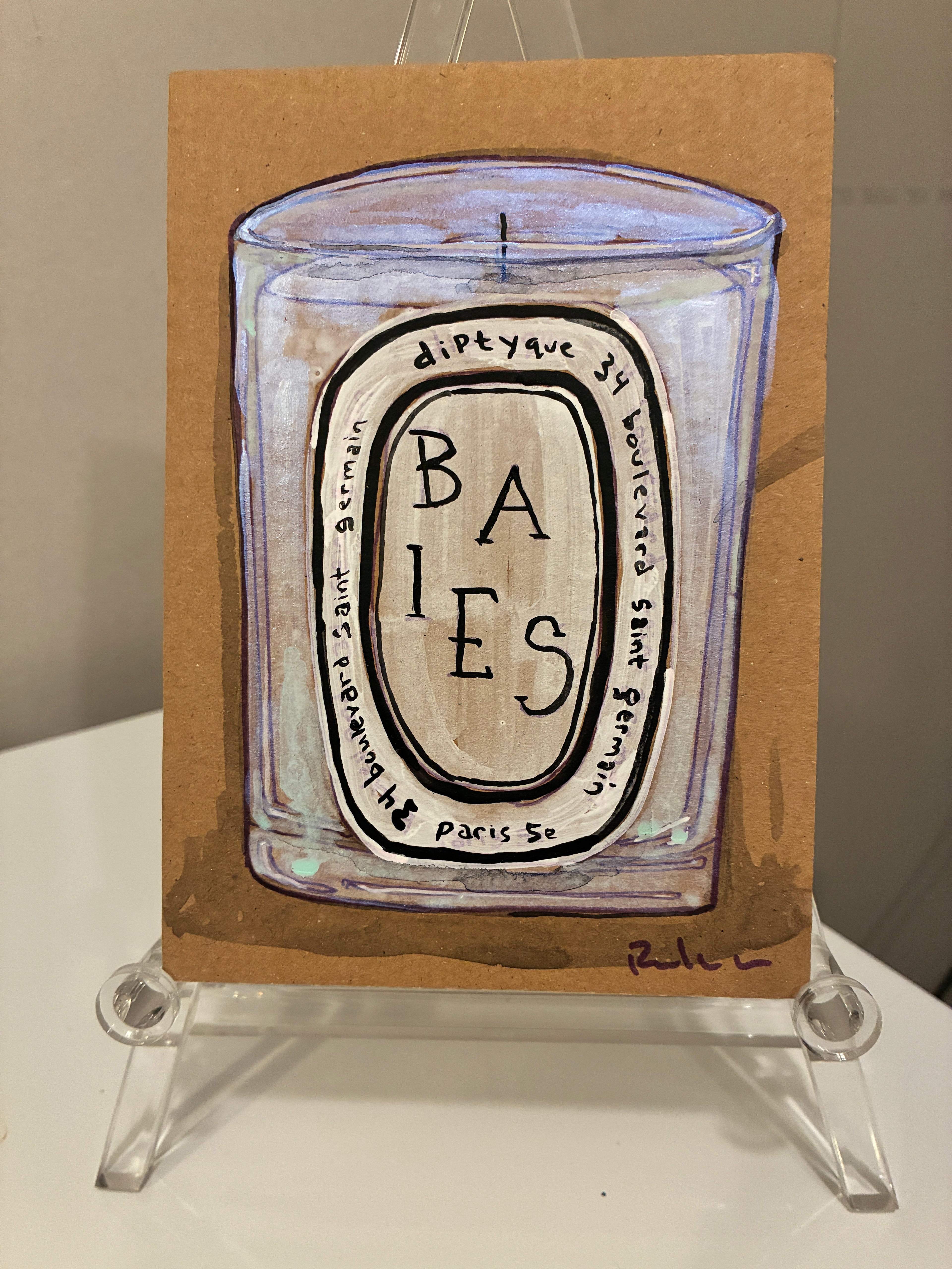 A hand-painted illustration of Rachel Nelson • Baies Paris by Thyne Goods on brown paper, shown upright on a clear stand. The candle label is visible, with the artist's signature at the lower right.