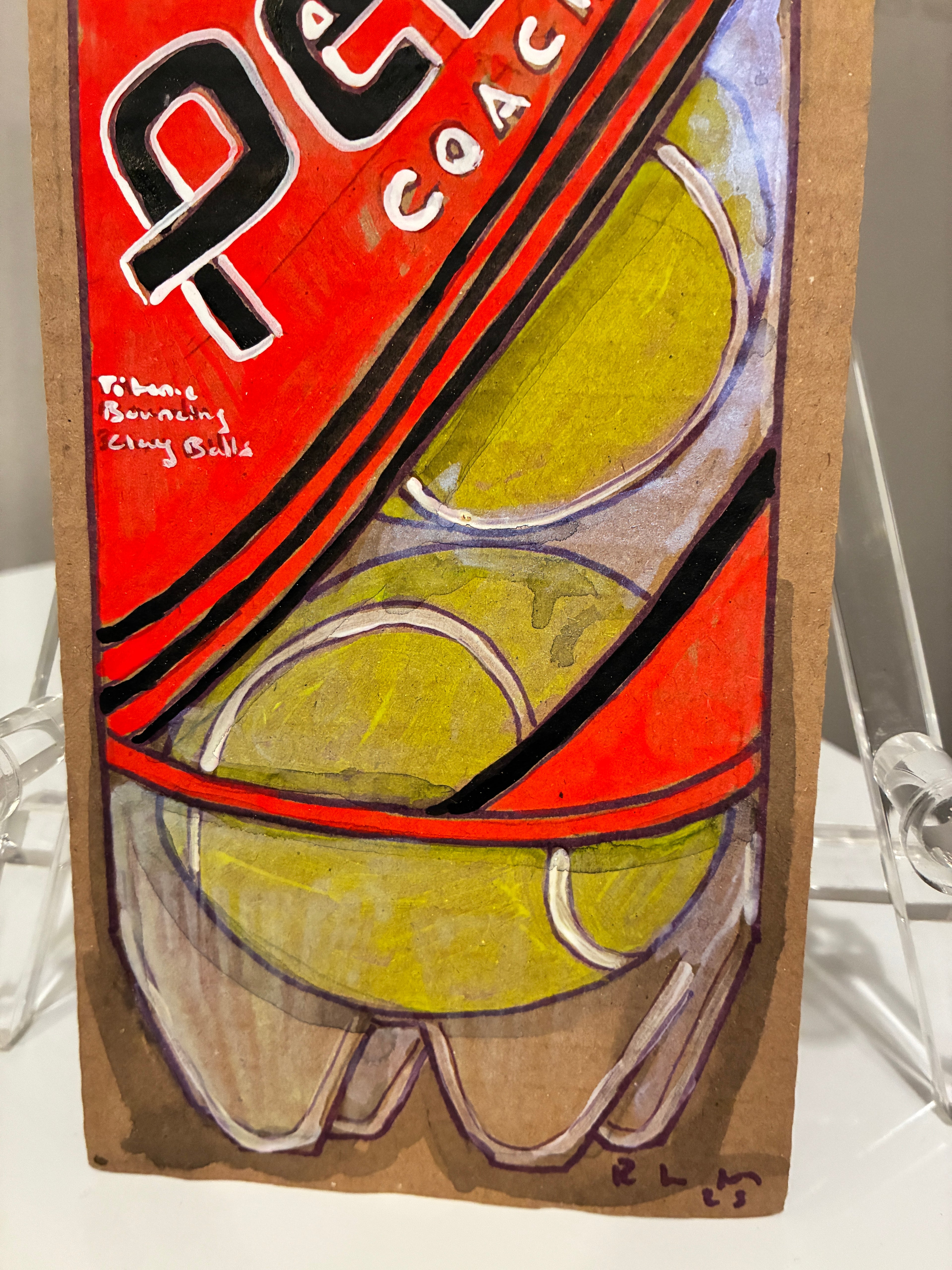 Rachel Nelson’s "Penn" for Thyne Goods is a vibrant cardboard artwork with two yellow-green tennis balls topped by a red and black label marked "COAC," reminiscent of neon flower paintings, with her signature and a handwritten note on the left.