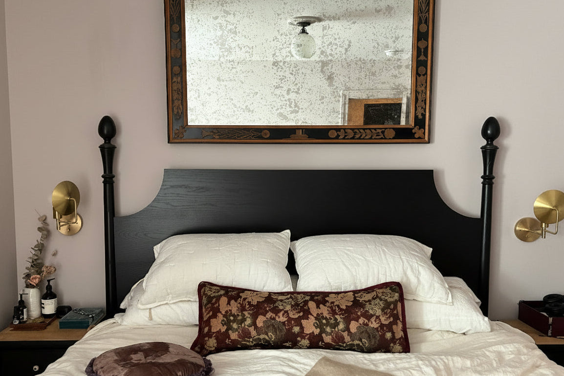 Bedroom with a large mirror above the bed, two wall sconces on either side, and decorative pillows.