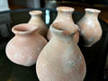 The HomArt Tiny Terra Cotta Vases - Set of 5 features small, round vases with narrow necks and a textured, weathered look. Arranged closely on a dark reflective surface, they showcase handcrafted charm for your decor.