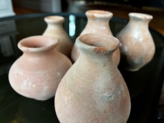 The HomArt Tiny Terra Cotta Vases - Set of 5 features small, round vases with narrow necks and a textured, weathered look. Arranged closely on a dark reflective surface, they showcase handcrafted charm for your decor.