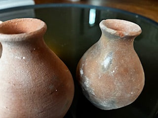 The HomArt Tiny Terra Cotta Vases - Set of 5 feature rustic, handmade charm with a weathered finish; two are displayed side by side on a reflective dark surface, highlighting their small, round shape and wide necks.