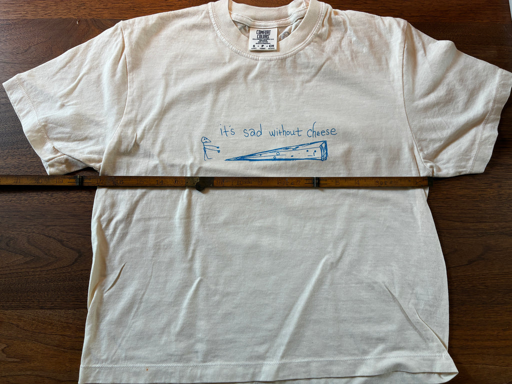 Thyne Goods' limited-edition Cheese cropped tee features a blue cheese wedge graphic and "Its sad without cheese." Printed on 100% cotton, it comes with a wooden ruler displayed horizontally across the front.