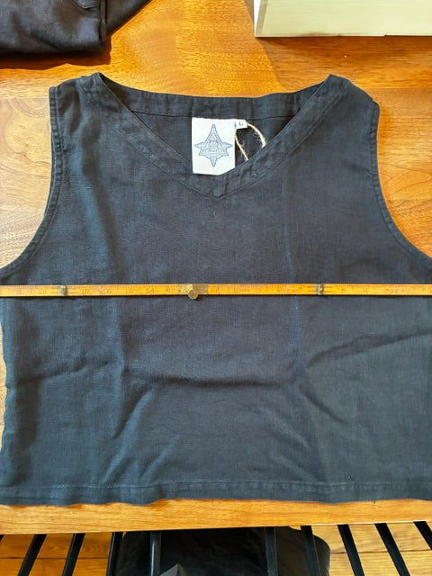 A Thyne Goods Basic Cami Tank in black is laid flat on a wooden surface with a measuring stick across the chest to show its width. A label with a star logo appears inside the neckline, and the top is made from 100% hemp.