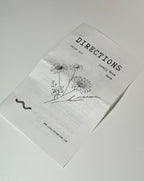 A folded paper titled DIRECTIONS with a delicate wildflower drawing, the words “Grief Kit,” “Lonely Work,” and “Pause,” along with a small snake illustration, evokes the thoughtful essence of the Grief Kit from Lonely Worm Farm—a heartfelt remembrance gift. The website www.lonelytower.com appears at the bottom, connecting back to Lonely Worm Farm’s brand.