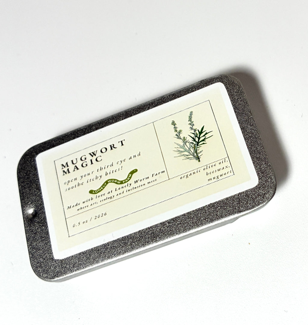 A rectangular tin labeled “Mugwort Magic from Lonely Worm Farm” by Thyne Goods features an illustration of mugwort. The light green and white label highlights the product’s eye and sleep benefits, with organic ingredients like mugwort and organic olive oil.
