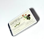 A rectangular tin labeled “Calendula Rose Lip Balm from Lonely Worm Farm” by Thyne Goods sits on a white background, featuring a floral illustration, ingredient list, and product details. This hydrating lip balm is enriched with organic olive oil and beeswax to naturally nourish and protect your lips.