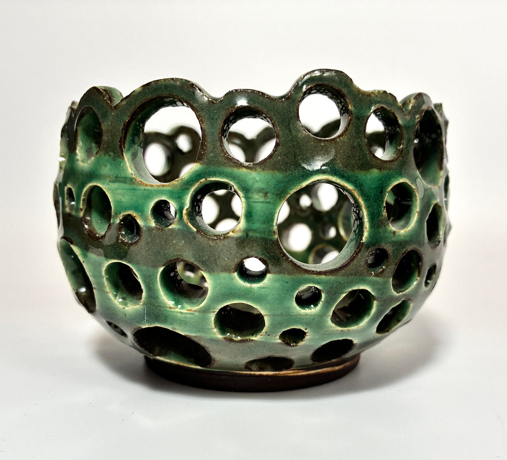 Introducing “Lettuce” by BMB: a green ceramic airplant bowl featuring numerous circular holes of varying sizes across its surface, creating an open and airy design. This handmade clay vessel is both functional and sculptural.