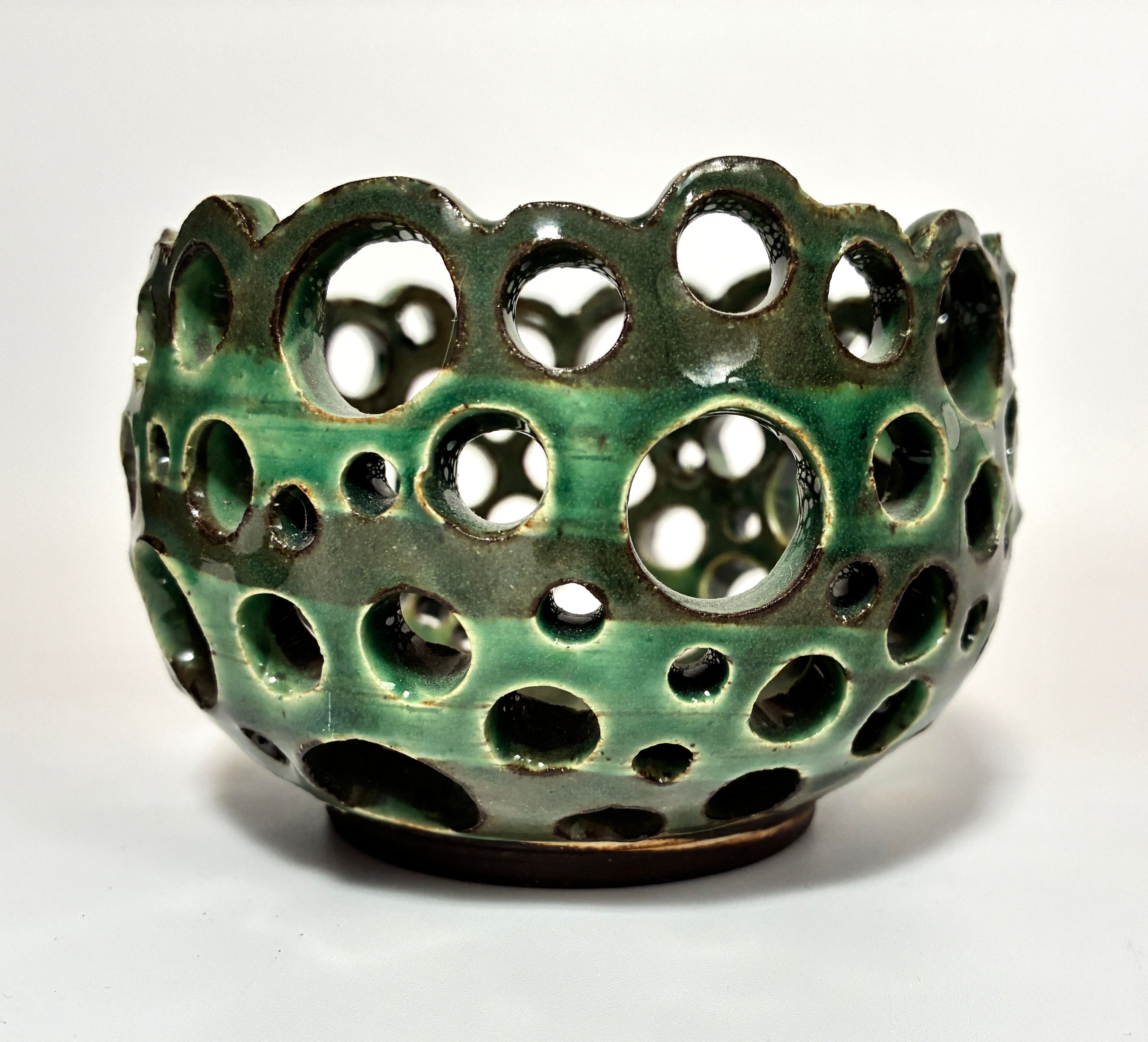 The BMB “Lettuce” is a round, green ceramic bowl featuring numerous circular holes of varying sizes throughout its walls—this distinctive artisan pottery piece is perfect for displaying airplants and is shown against a plain white background.