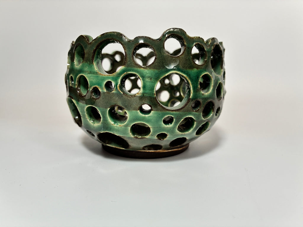 A round, green ceramic bowl named Lettuce by BMB, this handmade clay vessel features a glossy finish and multiple circular cutouts of various sizes—perfect for displaying airplants and elegantly showcased against a plain white background.