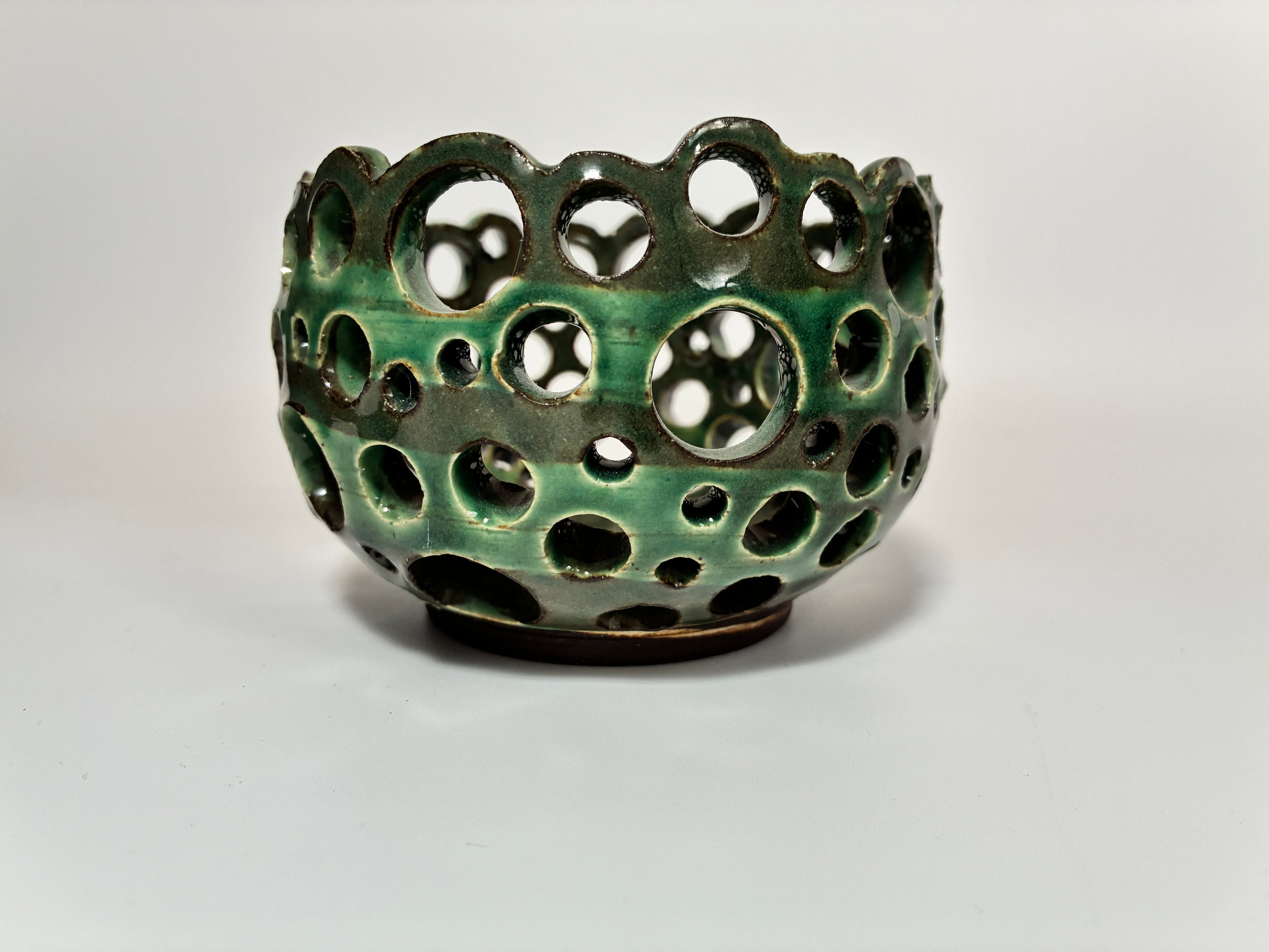 A round, green ceramic bowl named Lettuce by BMB, this handmade clay vessel features a glossy finish and multiple circular cutouts of various sizes—perfect for displaying airplants and elegantly showcased against a plain white background.