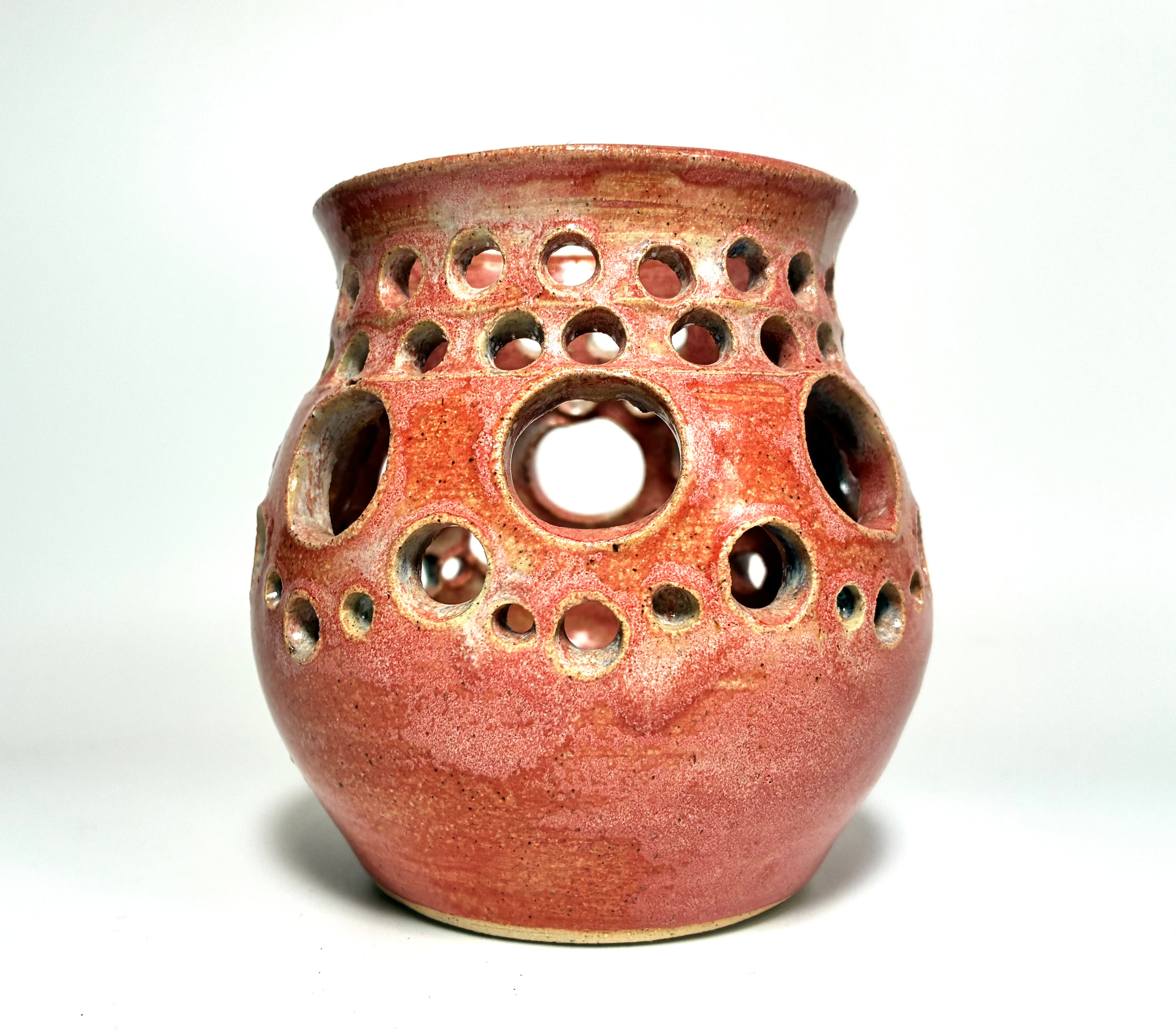 A ceramic vase named “Spam” by Thyne Goods, crafted from clay with a glossy red finish and featuring multiple round holes of varying sizes across its body, is displayed against a plain white background.