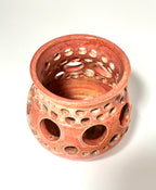 A reddish-brown clay ceramic vase, named Spam by Thyne Goods, with circular holes of various sizes covering its sides, viewed from above on a white background.