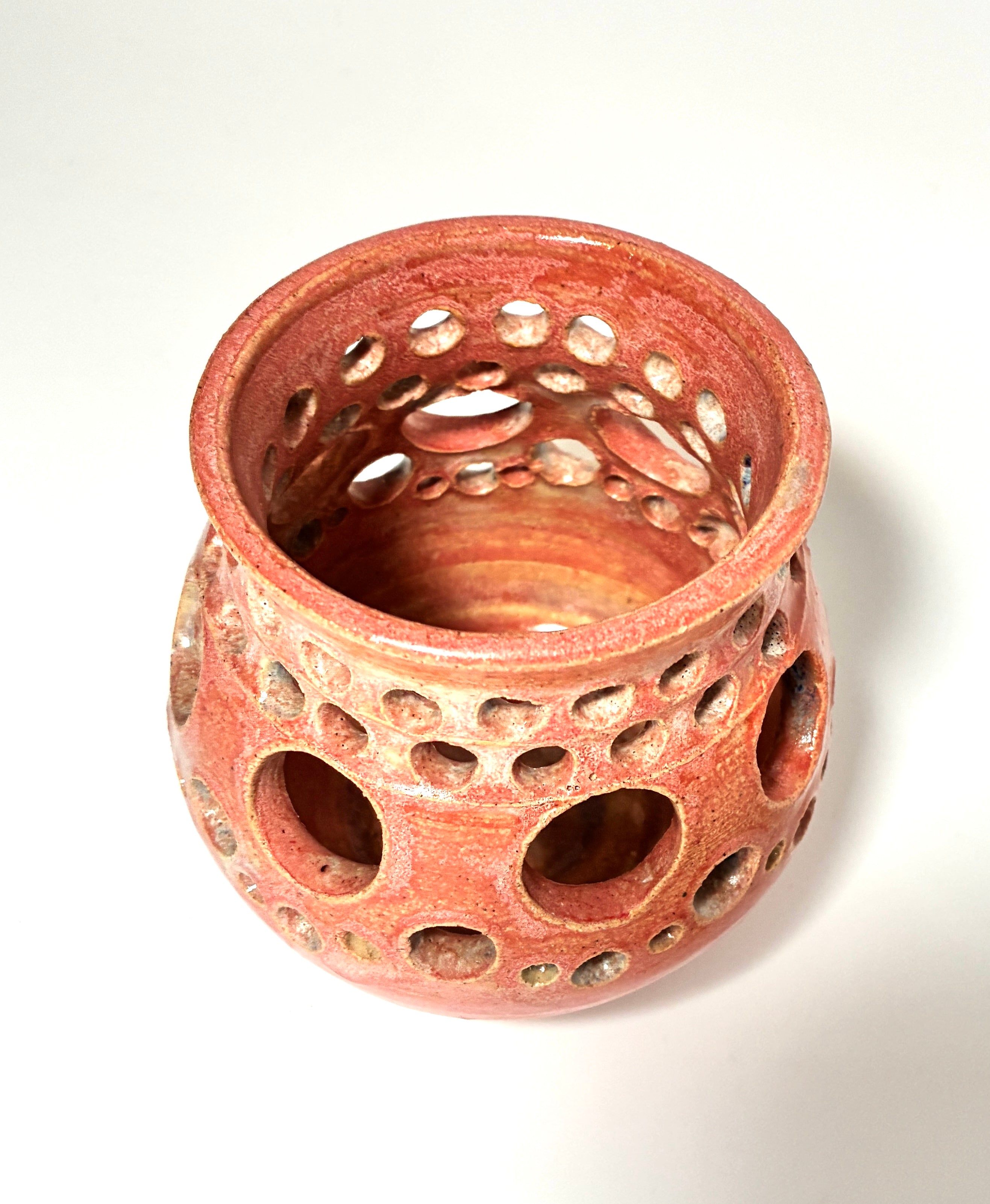 A reddish-brown clay ceramic vase, named Spam by Thyne Goods, with circular holes of various sizes covering its sides, viewed from above on a white background.
