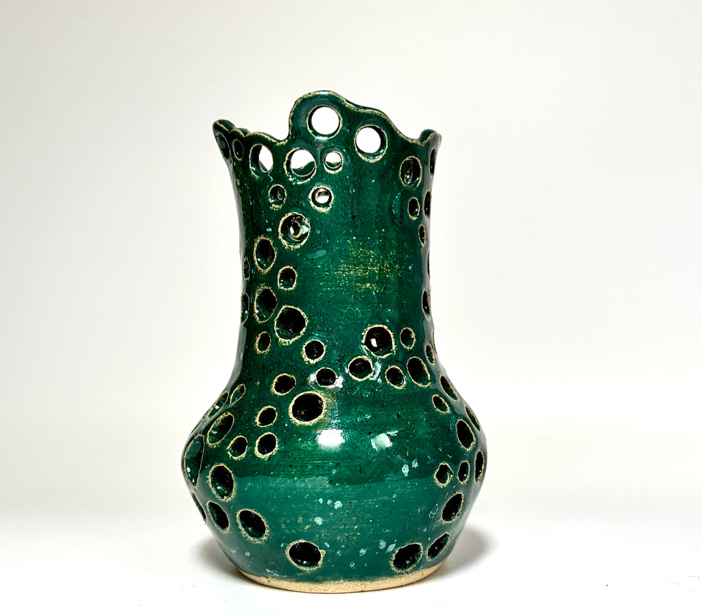 A green ceramic vase with a glossy glaze and a decorative pattern of circular cutouts, photographed against a plain white background.