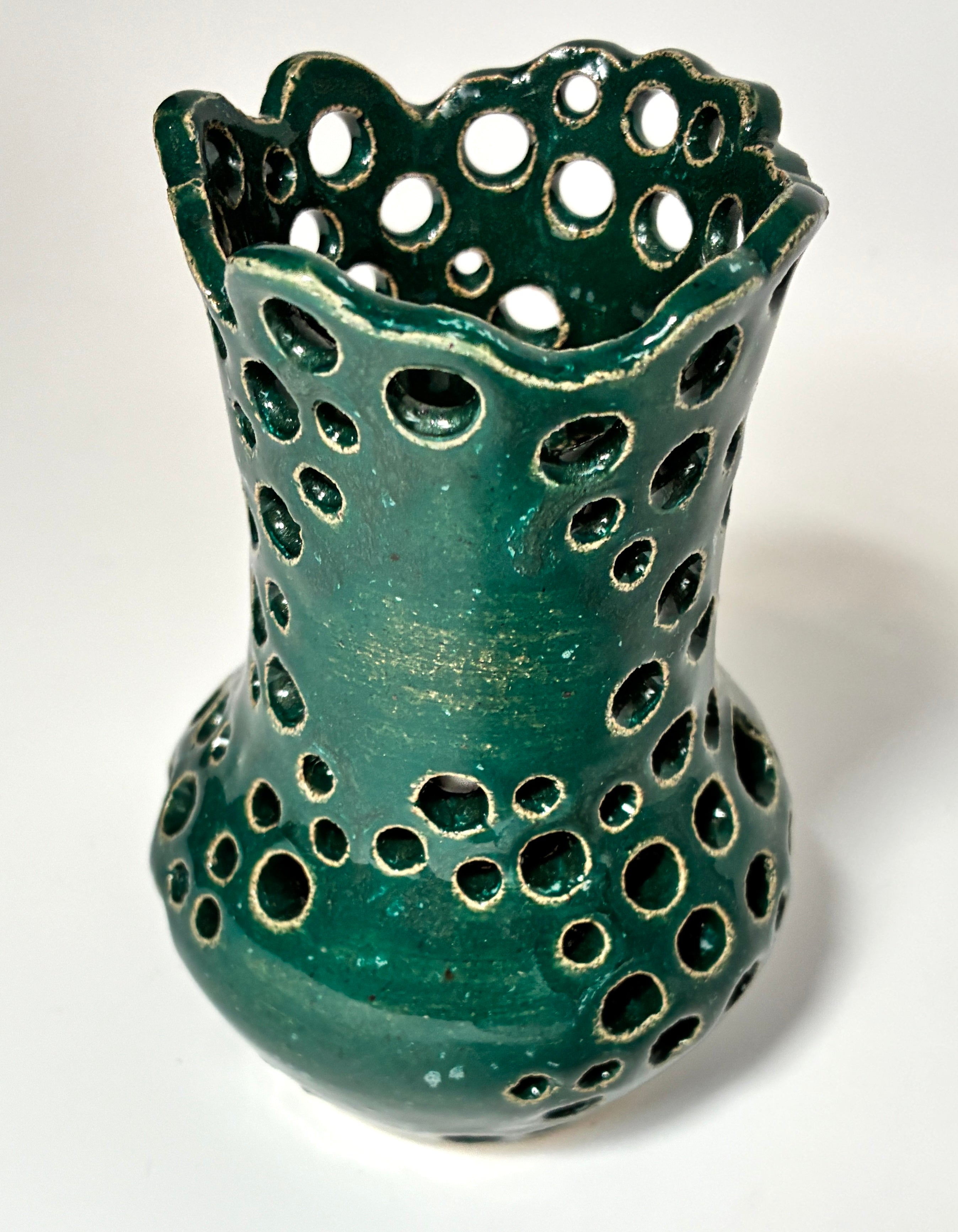 A green ceramic vase with a scalloped rim and numerous circular cutouts, showcasing a glossy glaze with subtle gold-toned distressing, set against a plain white background.