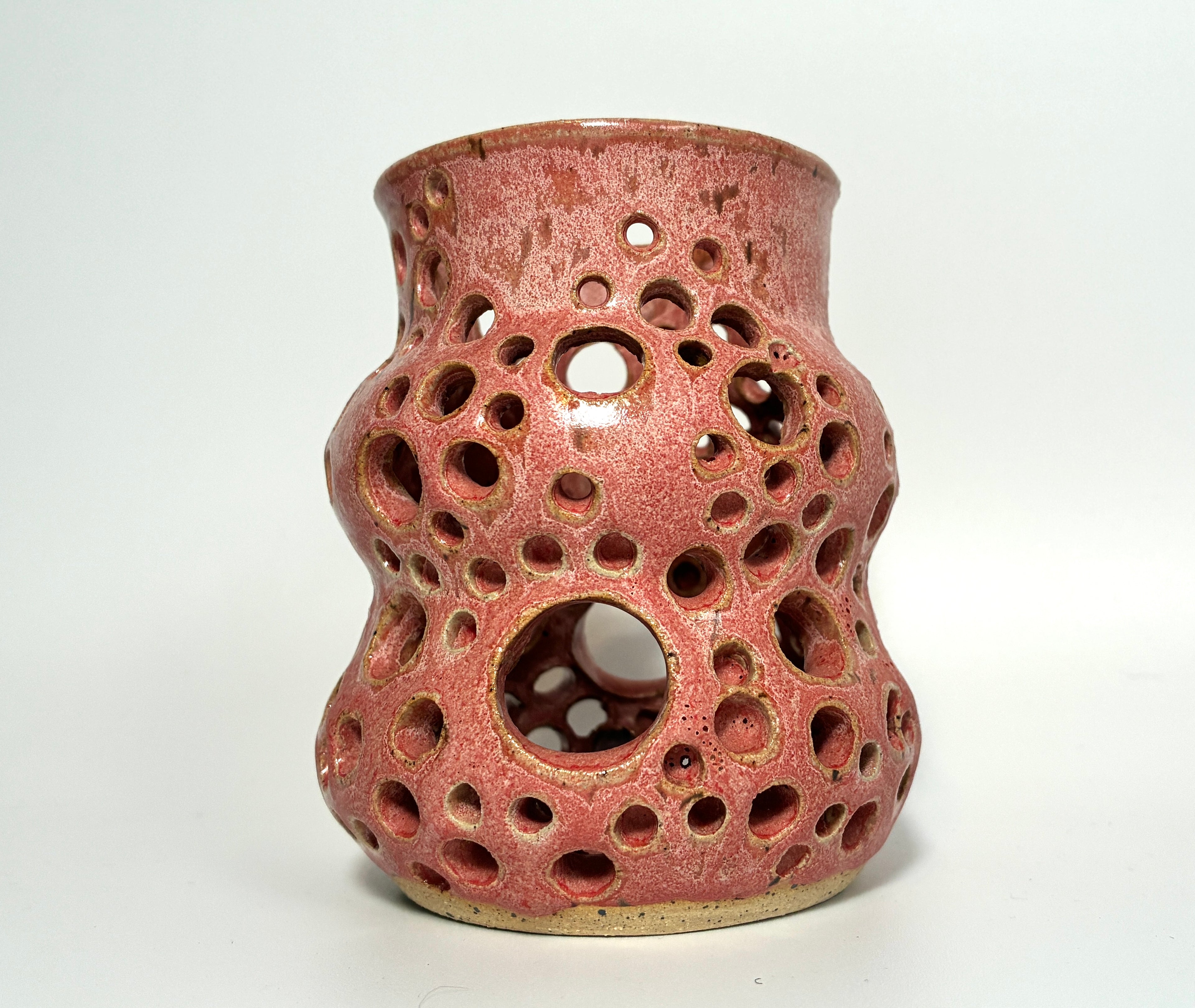 The Spamalot by BMB is a pink ceramic vase with a glossy finish, featuring numerous circular holes of varying sizes handcrafted throughout its surface, and is photographed against a plain white background.