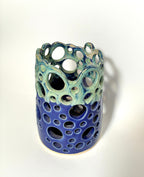 A cylindrical handmade clay vase from the BMB Widow’s Bay collection, featuring circular cutouts and glazed with blue on the bottom half and green on the top, set against a plain white background.