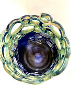A top-down view of the one-of-a-kind Widow’s Bay decorative glass by BMB, featuring a blue center and a textured, greenish rim with oval cutouts arranged in a circular pattern.