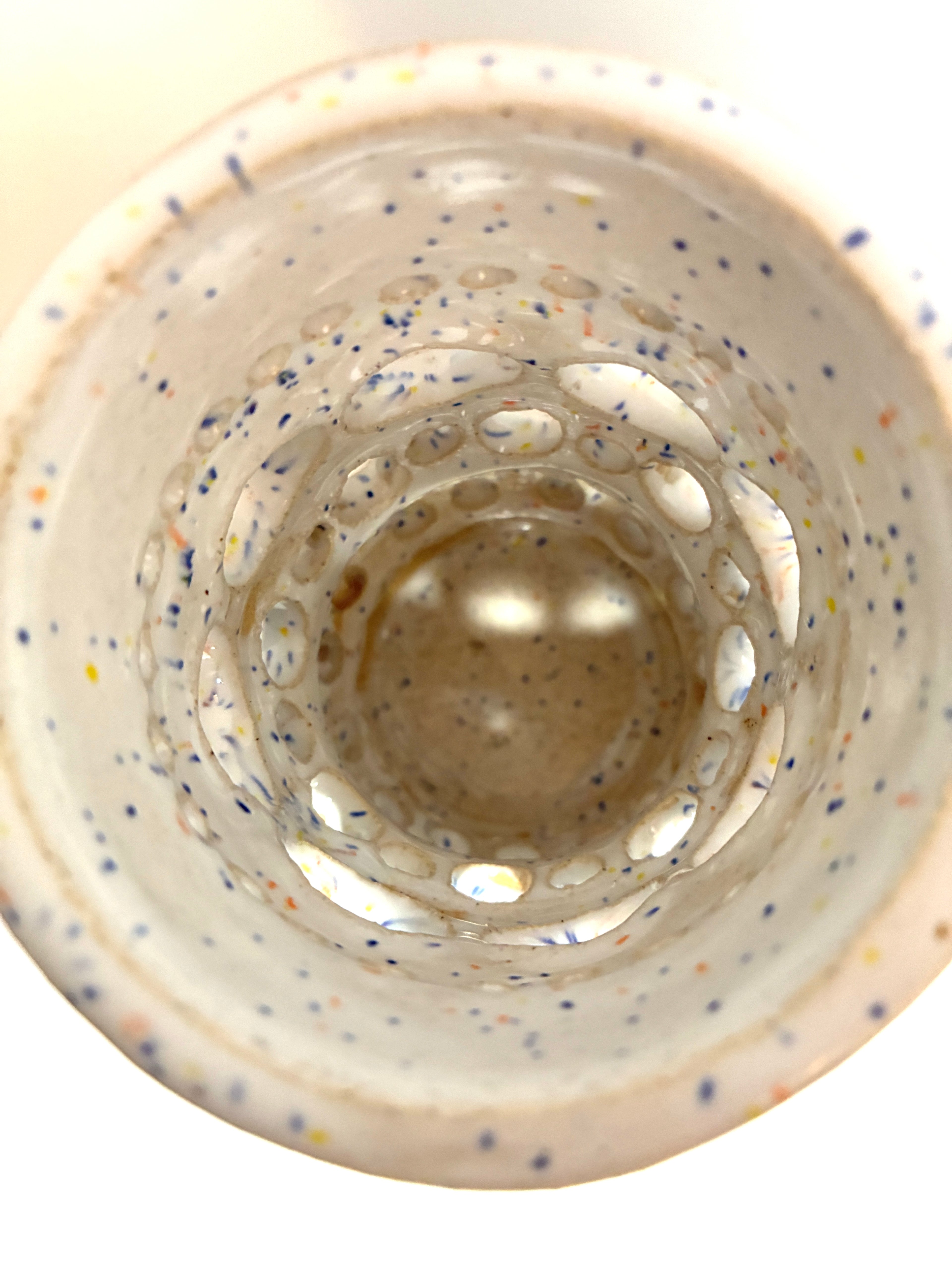 View from above of Apogee by BMB—a white ceramic cup featuring a speckled pattern and textured, circular indentations inside that create a layered, tunnel-like effect. This eye-catching home accessory pairs beautifully with any handmade clay vase or dried flower vessel.