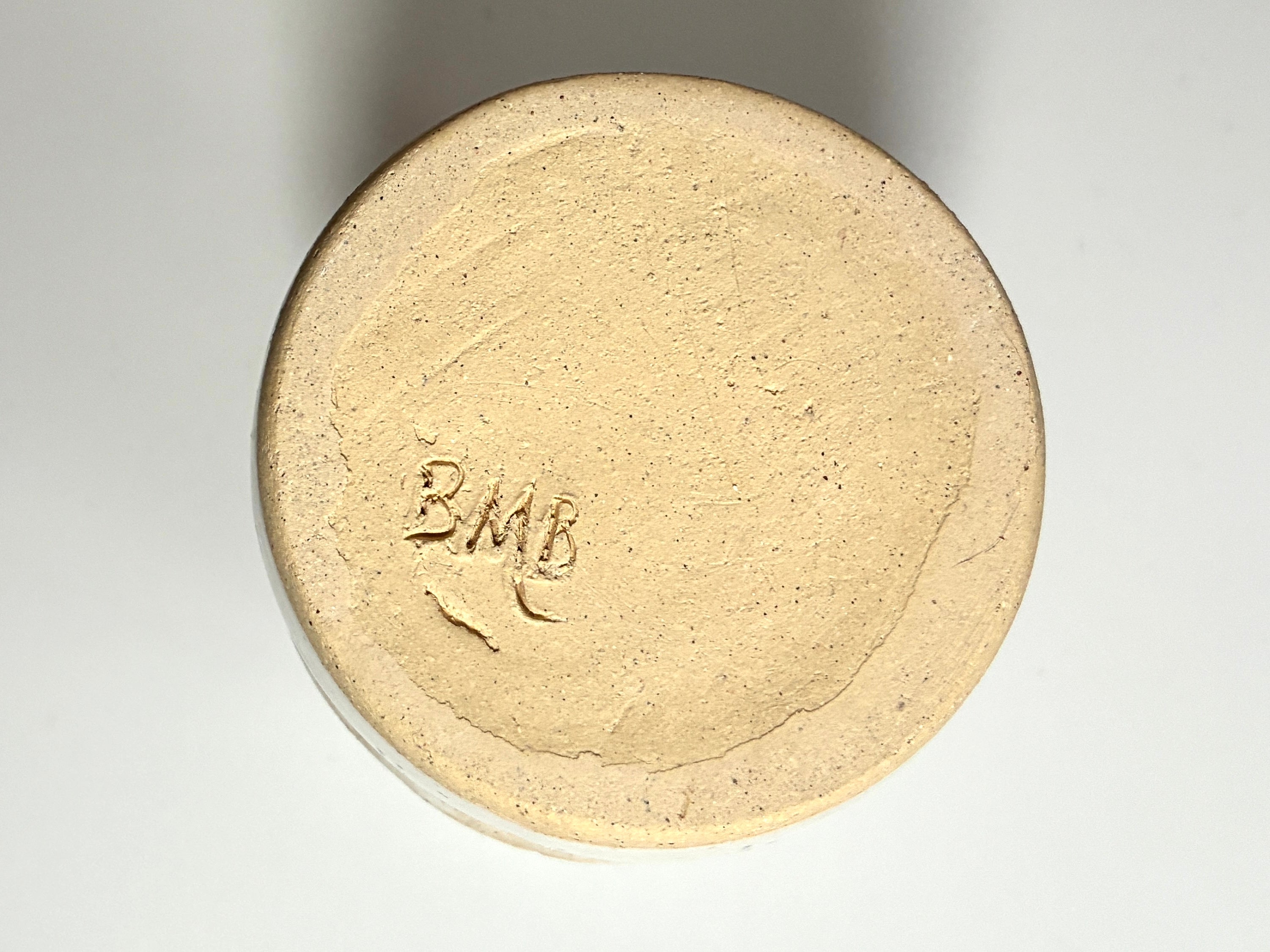 A top view of the Apogee vase by BMB—a round, beige ceramic piece with “BMB” inscribed at its center—showcasing its elegant, handmade craftsmanship on a plain white background; this stylish home accessory is perfect for use as a dried flower vessel.
