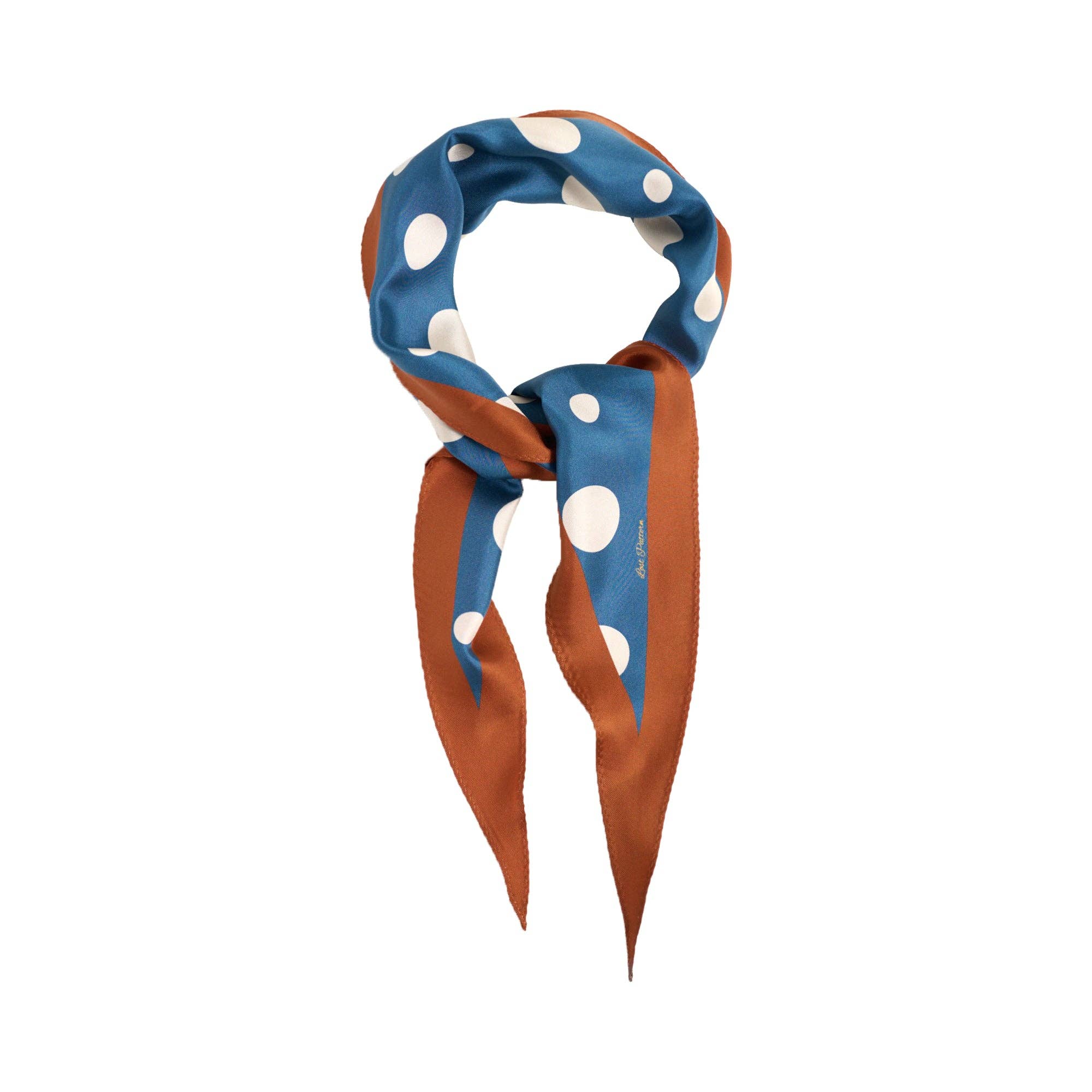 The Lost Pattern NYC Silk Polka Dot Diamond Neckerchief in Salted Caramel, featuring a blue and white polka dot design with brown edges and pointed ends, is tied in a loose knot on a plain white background.