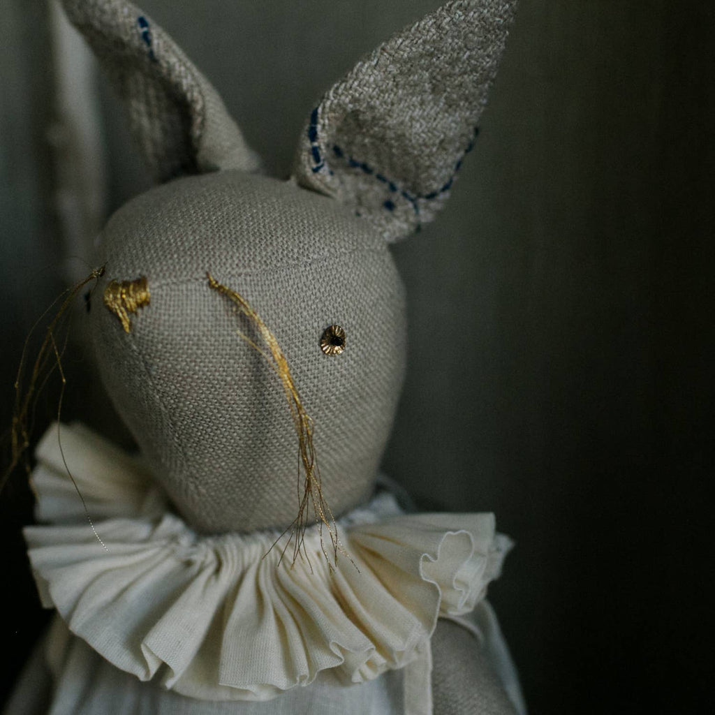 The Skippy Cotton Ruffle Bun Ragdoll is a handmade cotton-filled art doll featuring hand-stitched details, embroidered face, tall ears, and a white ruffled collar—a charming decorative hare for any space.
