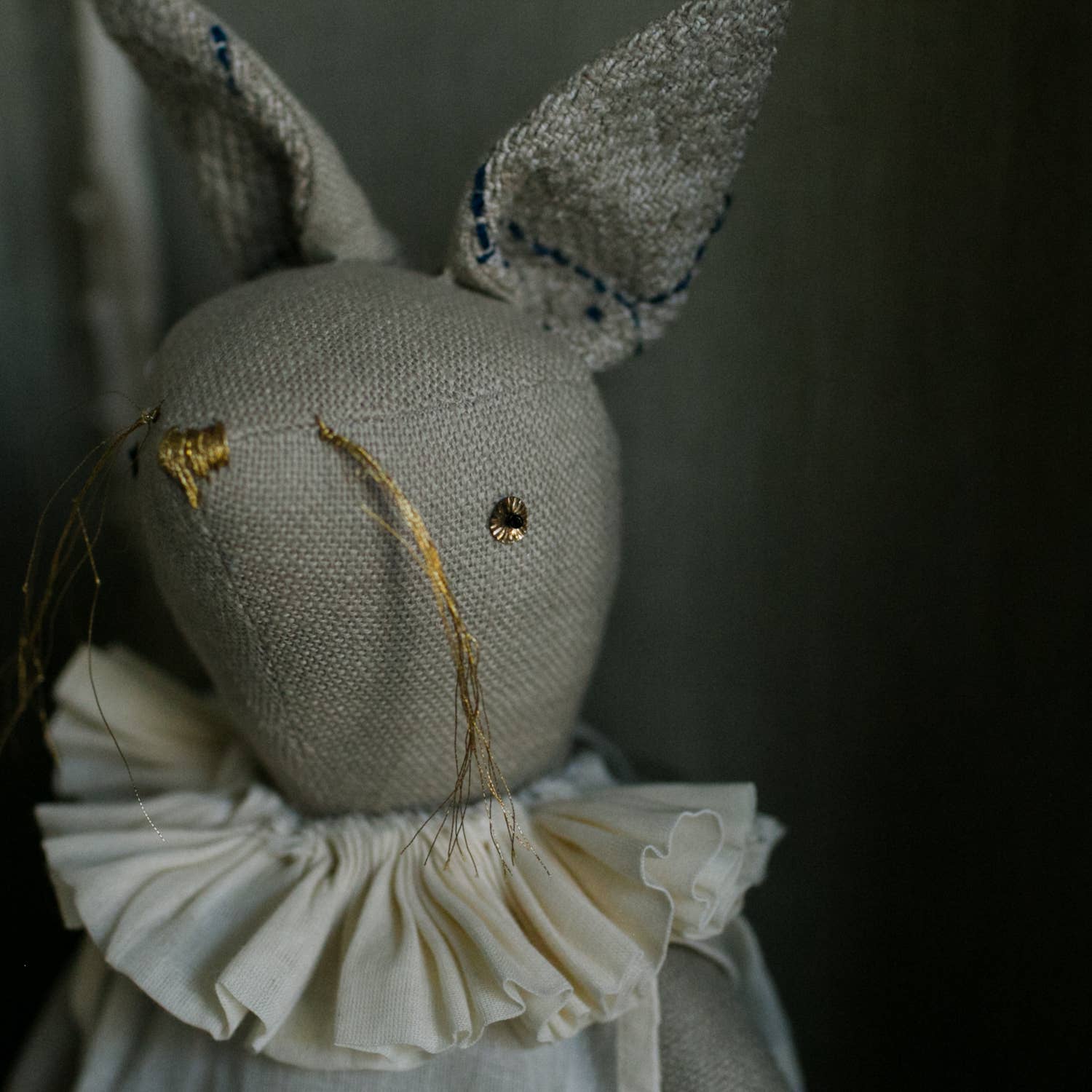 The Skippy Cotton Ruffle Bun Ragdoll is a handmade cotton-filled art doll featuring hand-stitched details, embroidered face, tall ears, and a white ruffled collar—a charming decorative hare for any space.
