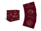 A burgundy deck box titled *Spells: A Little Deck of Enchantments* by Lorriane Anderson from Simon & Schuster is shown, along with three matching flashcards featuring intricate gold designs and spells such as Self-Love and More Money—perfect for anyone seeking witchy inspiration or interested in spellcraft.