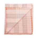 A Silica Rose Throw by Variously, featuring shades of salmon and gray in a stripes pattern, neatly folded with one corner flipped over to show both sides of the fabric.