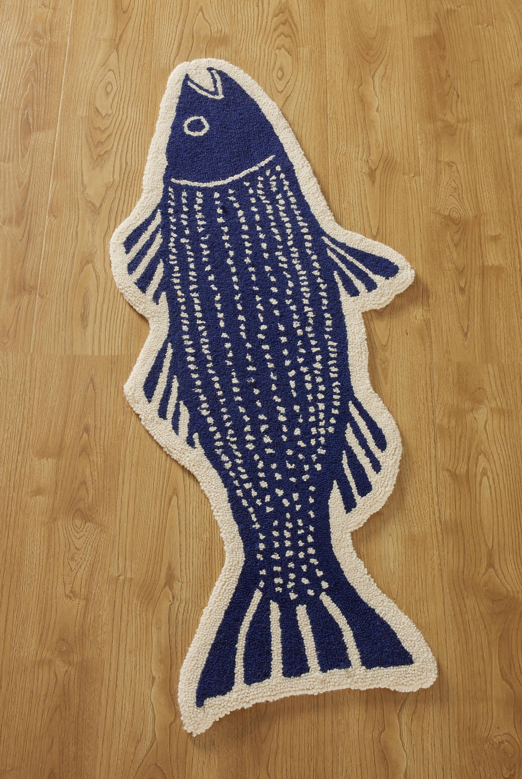 The Striper Shaped Hook Rug by Kate Nelligan for Peking Handicraft, with blue and white fish details including fins, tail, and eye, adds charm to your entryway when placed on a wood-patterned floor.