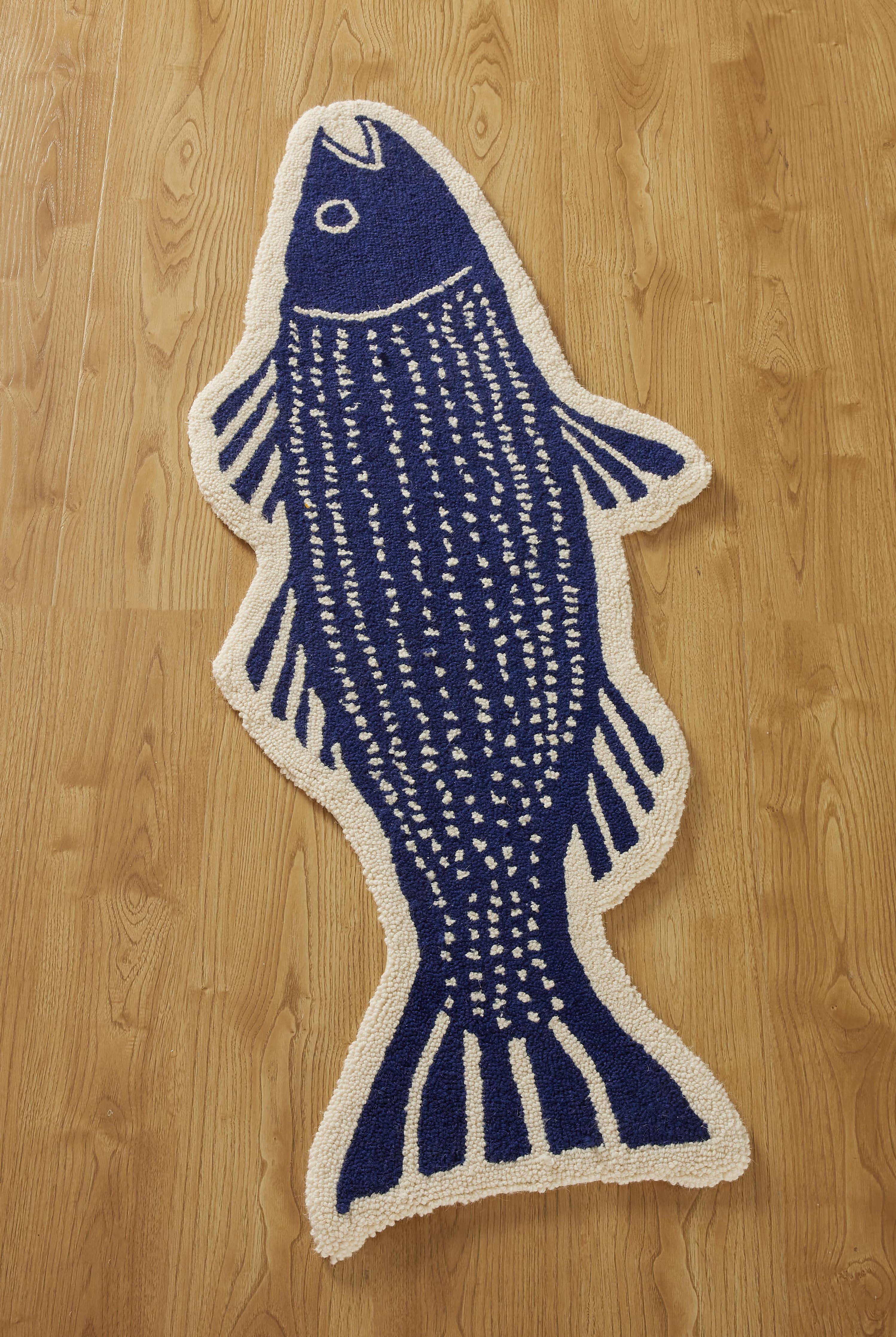 The Striper Shaped Hook Rug by Kate Nelligan for Peking Handicraft, with blue and white fish details including fins, tail, and eye, adds charm to your entryway when placed on a wood-patterned floor.