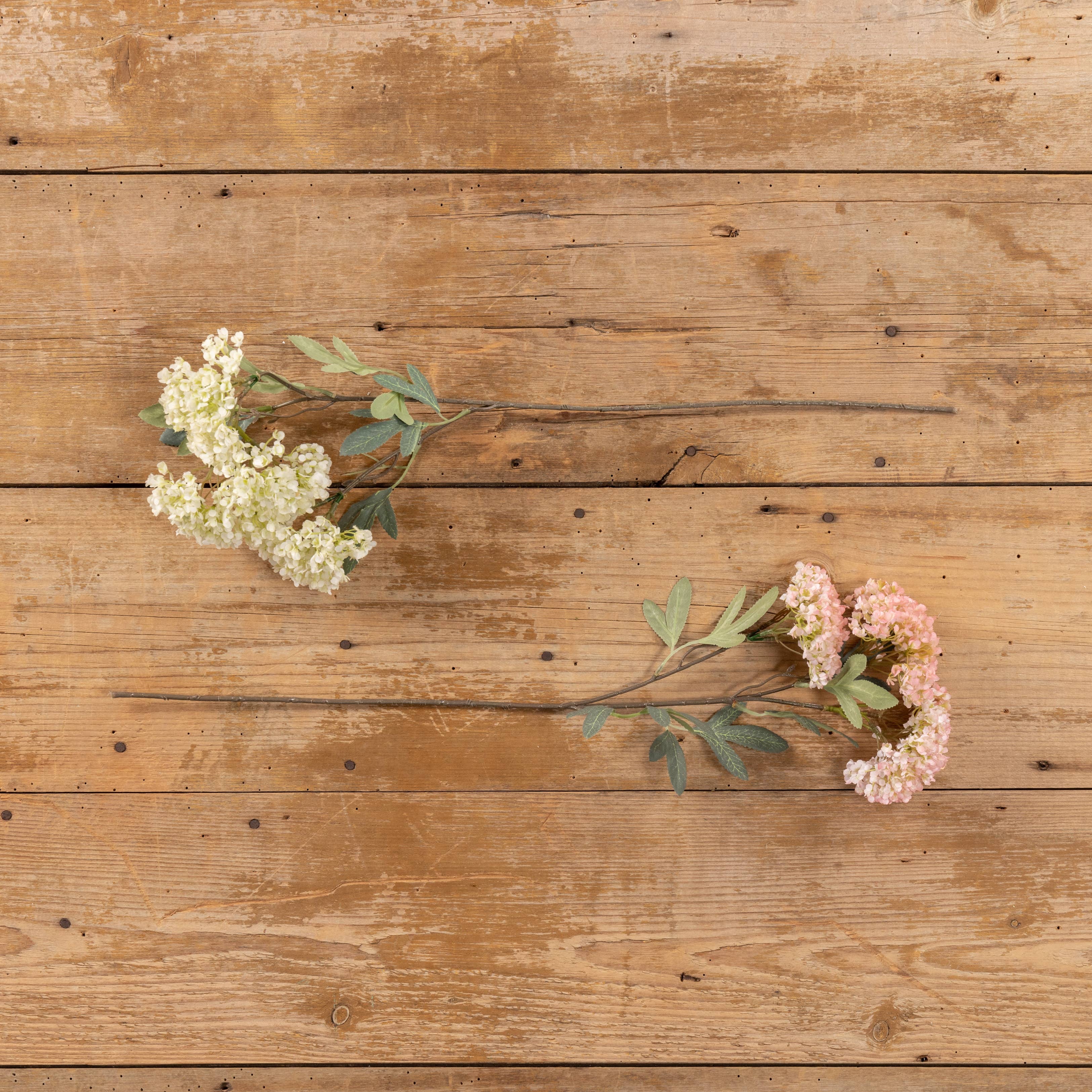 A 25" PINK FAUX HYDRANGEA SPRAY by Ragon House is arranged with white and pink blooms on a rustic, light brown wooden surface with visible grain and knots.