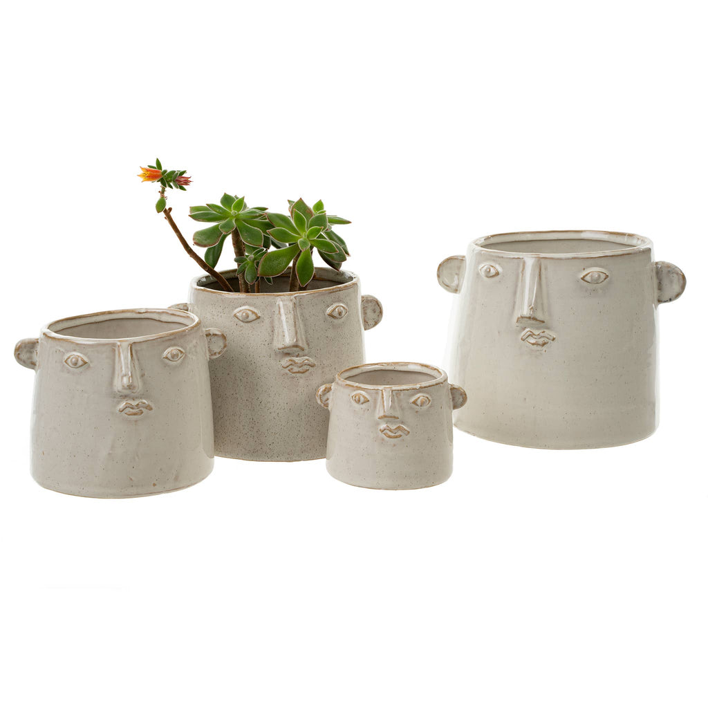 The Character Pot L by Indaba Trading includes four off-white ceramic face-shaped planters with sculpted features and ears. One holds a mini succulent with an orange flower; the rest are empty. Pots have no drainage holes.