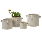 The Character Pot L by Indaba Trading includes four off-white ceramic face-shaped planters with sculpted features and ears. One holds a mini succulent with an orange flower; the rest are empty. Pots have no drainage holes.