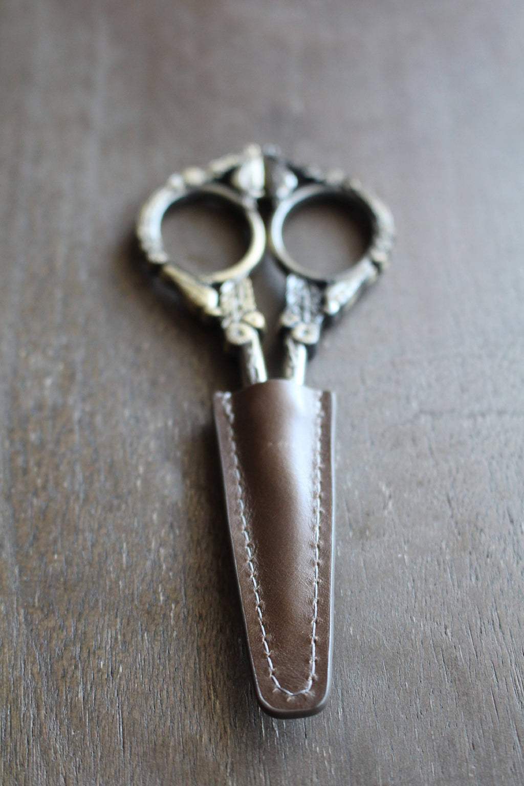 The NNK Press Leather Scissor Sheath protects your embroidery scissors with style—an elegant accessory that keeps your ornate tools safe and organized on any crafting surface.