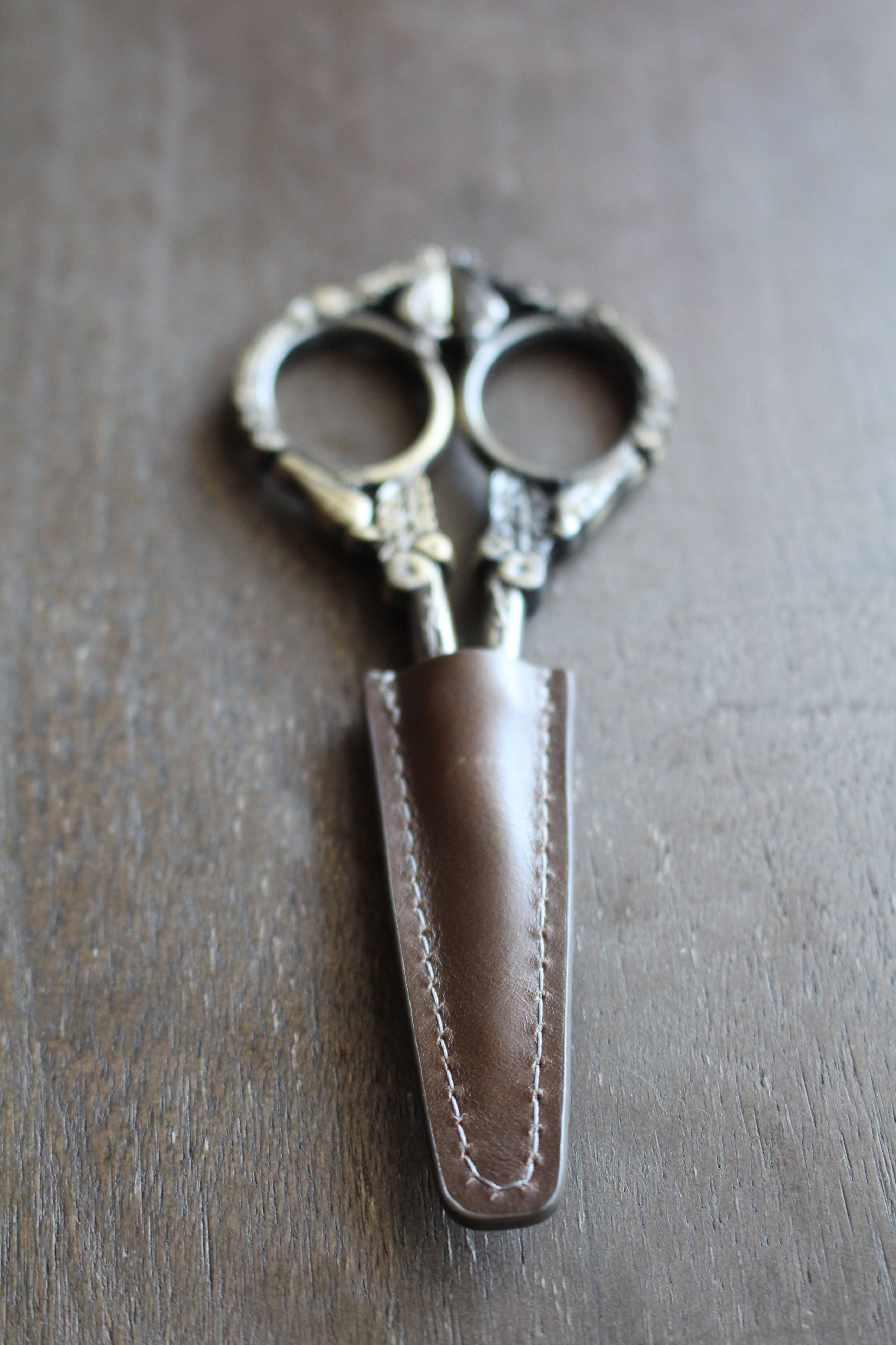 The NNK Press Leather Scissor Sheath protects your embroidery scissors with style—an elegant accessory that keeps your ornate tools safe and organized on any crafting surface.