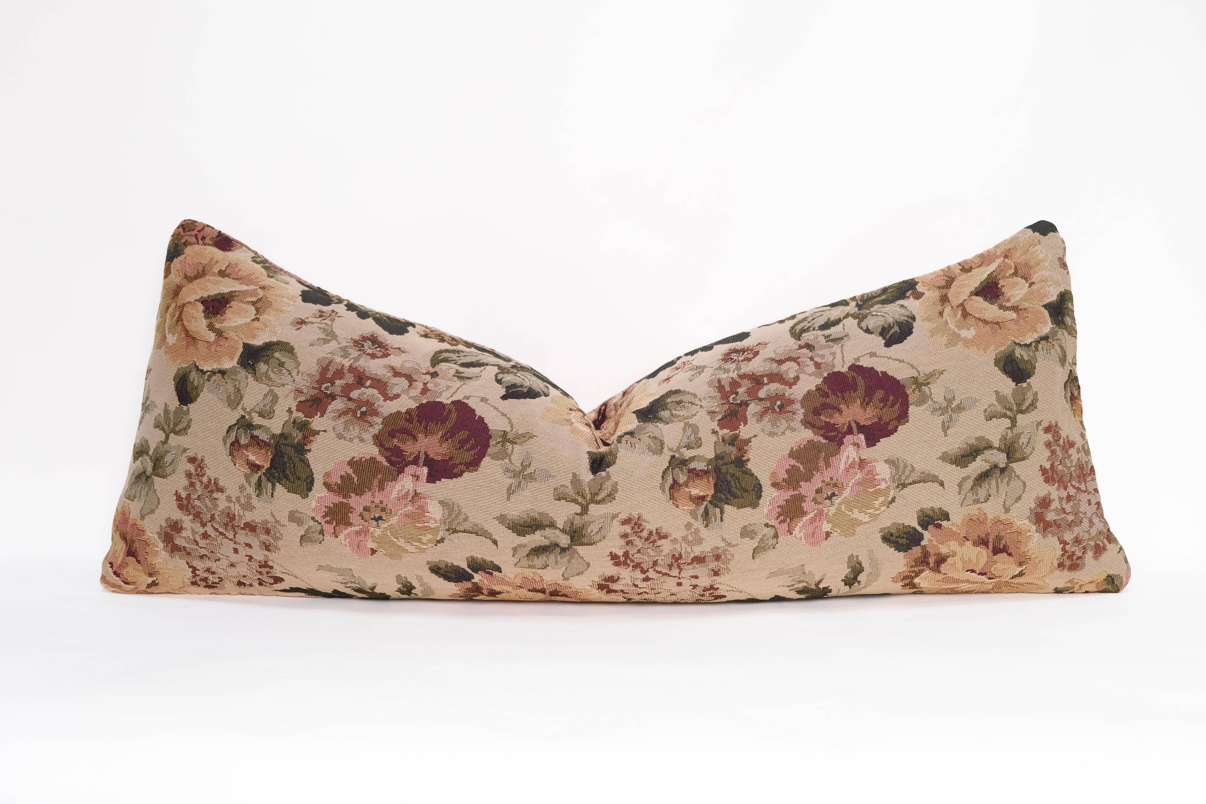 The Tapestry Long Lumbar pillow by Twenty Third by Deanne features a decorative jacquard floral pattern in brown, pink, green, and beige on a plain white background.