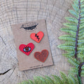 The ilikesara | art + goods Iron-on patch | heart 3-pack - red features three unique embroidered heart patches, each with a distinct design, displayed on a brown card alongside green fern leaves.