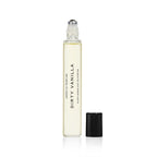 A clear 10ml rollerball bottle of DIRTY VANILLA by Heretic Parfum, a vanilla fragrance with amber notes, stands upright with its silver roller tip exposed and black cap beside it on a white background.