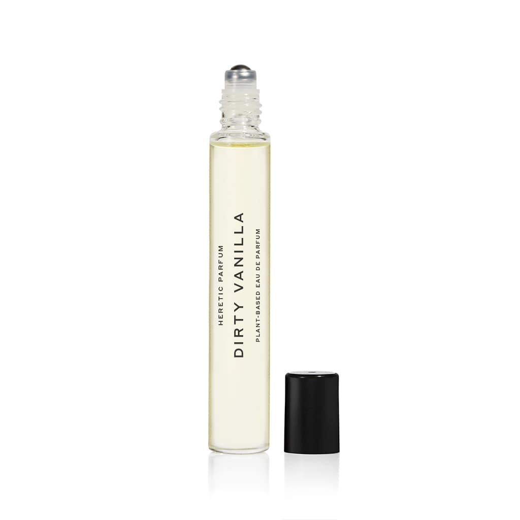 A clear 10ml rollerball bottle of DIRTY VANILLA by Heretic Parfum, a vanilla fragrance with amber notes, stands upright with its silver roller tip exposed and black cap beside it on a white background.