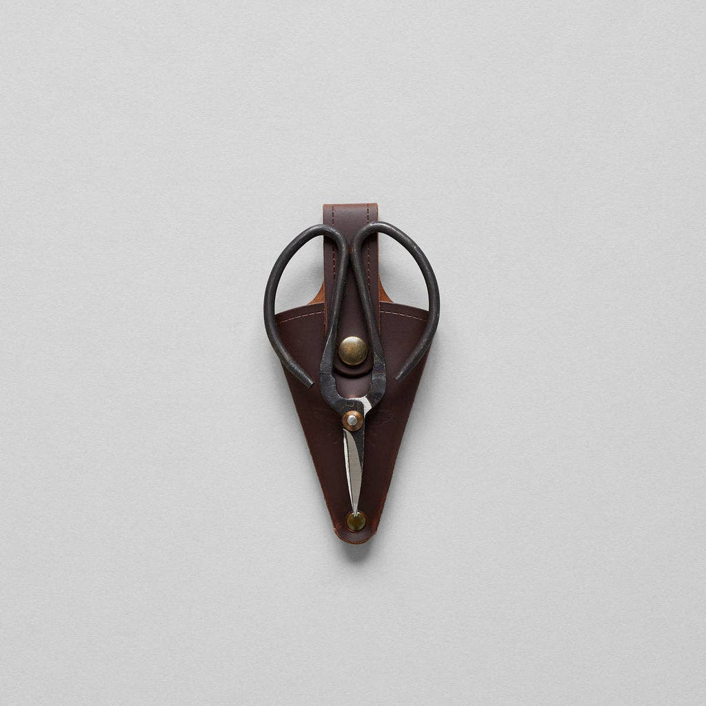 The Bloomist Gardener's Planting Set (One Size) features black metal floral scissors in a brown leather sheath with a brass button, displayed on a light gray background—a refined essential for any gardening collection.